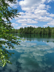 The shore of the lake Light with turquoise water, which reflects the trees and the sky with clouds, in the mountain park Ruskeala.