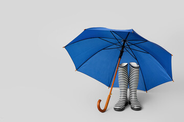 Stylish umbrella with gumboots on light background
