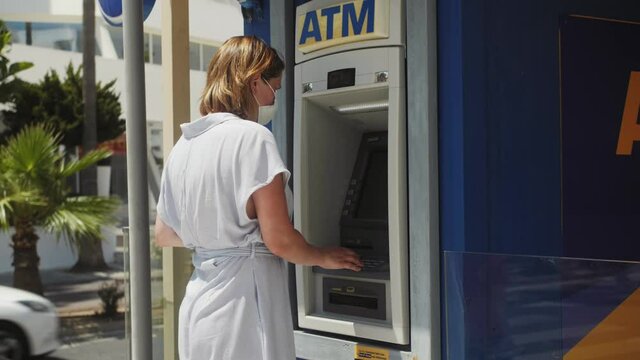 Tourist in medical mask using credit card in atm for cash withdrawal during pandemic. Financial security and banking system concept. Banking service, transfer and cash withdrawal concept.
