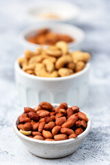 Types of nuts in white ceramic bowls. Almond, cashew, peanut ground. Food vertical high key photo. Vegan vitamin products.