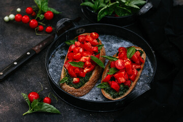 sandwiches with pesto and tomatoes on black bread on a dark background