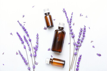 Bottles of lavender essential oil and flowers on light background