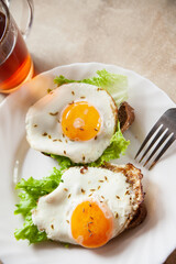 Delicious toasts with fried eggs and lettuce leaves for breakfast placed on table near cup of hot tea in morning