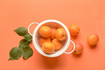 Colander with tasty ripe apricots on color background