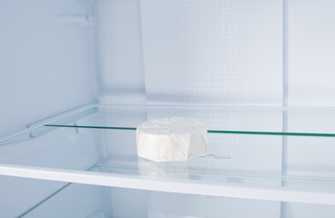 Obraz na płótnie Canvas against the background of a white refrigerator, brie cheese in a closed package is lying on a glass shelf, close-up