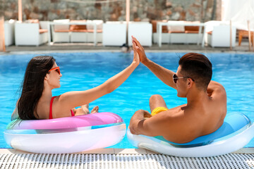 Young couple with inflatable rings giving each other high-five in swimming pool