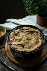 Unbaked meat (sausage ), mushroom, cheddar and rosemary spelt pie decorated with crust leaves in baking tin on old wooden table.