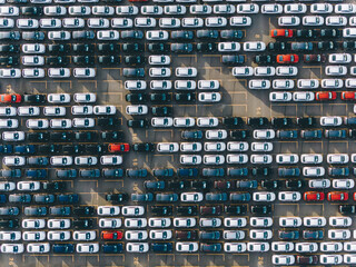 Open finished automobile warehouse of giant plant with rows of cars of different colours casting shadows in bright morning aerial view