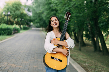 A charming guitarist hugs her favorite instrument during a walk in the summer park. Summer time,...