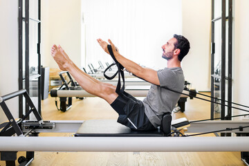 Fit muscular man doing a teaser pilates exercise on a reformer