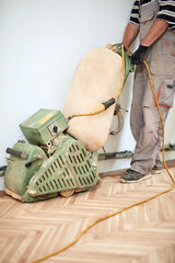 Repairman restoring parquet with a sanding machine.