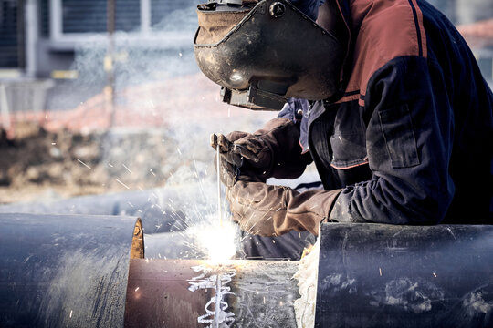 Construction worker arc welding the metal pipe.