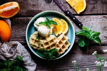 Belgian waffles with orange and ice cream on a wooden table