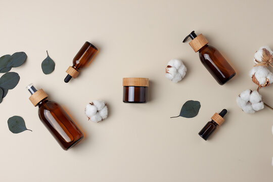 Cosmetic skin care products with flowers and eucalyptus on pastel beige background. Flat lay, copy space