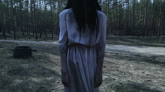 Girl in image of scary zombie stands near stone well among forest.
