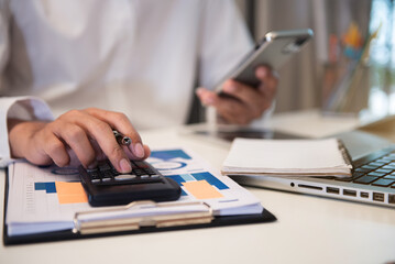 Fototapeta premium Close up male hand using calculator and smartphone calculate about cost at home office.