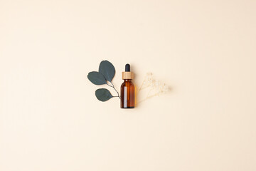 Cosmetic bottle with flowers and eucalyptus on pastel beige background. Flat lay, copy space