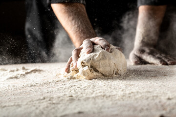 White flour flying into air as pastry chef in white suit slams ball dough on white powder covered...