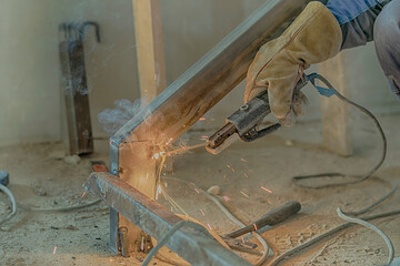 Cropped male hands of a worker with a welding machine. Installation of a metal structure by welding. Sparks of hot metal are flying.