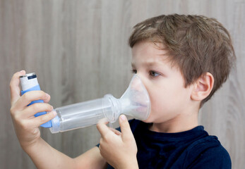 Child boy using medical spray for breath. Inhaler, spacer and mask. Side view - obrazy, fototapety, plakaty