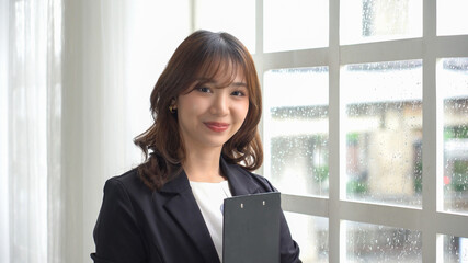 Asian woman holding a note near a window on a rainy day. (Chinese, Japanese, Korean or Thai)