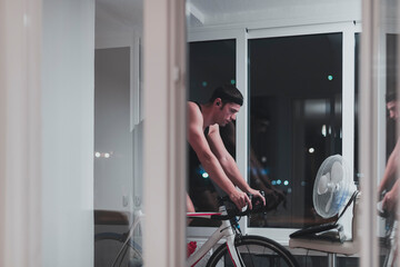 Fototapeta na wymiar Man cycling on the machine trainer he is exercising in the home at night playing online bike racing game