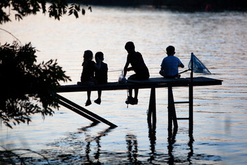 Silhouette of children fishing in the river Meuse from a jetty  in Geijsteren in the North of Limburg