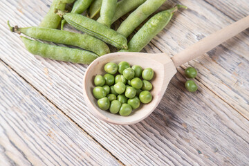 Top view of a wooden spoon with green peas and pods on a bright table. The concept of vegan products
