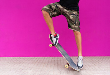 View of man legs performing a trick with skateboard on pink background.