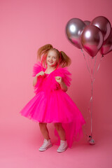 Obraz na płótnie Canvas little girl on a pink background holding balloons, celebrating her birthday