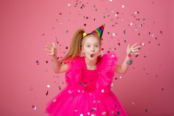 Obraz na płótnie Canvas a little girl on a pink background blowing confetti celebrates her birthday