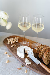 Two glasses of white wine and a wooden board with appetizers on the table.