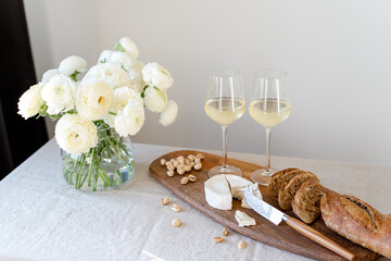 Two glasses of white wine and a wooden board with appetizers on the table.