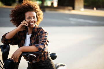 Beautiful african girl talking to the phone. Happy young woman driving electric bicycle