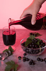 A woman's hand pours homemade blackcurrant liqueur into a glass from a decanter. Low key