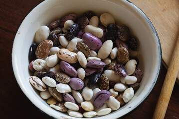 Close up of multicolored beans in an enamel cup put on a wooden table