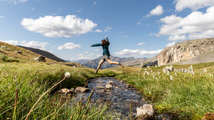 Une jeune fille saute au dessus d'une rivière avec une jolie vue en arrière plan. 