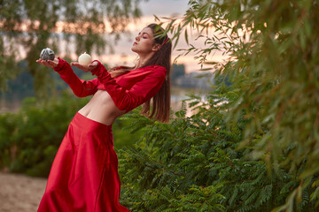 Ritual dance with candles in hands. Brunette woman in red costume for belly-dance is dancing on the beach