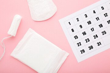 White calendar and new pack of sanitary towel, panty liner and tampon on light pink table...