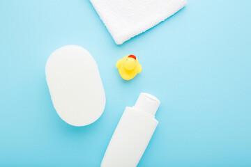 White shampoo bottle, towel, wisp and yellow rubber duck on light blue table background. Pastel color. Closeup. Things for baby bathing. Top down view. © fotoduets