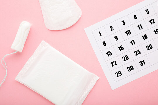 White calendar and new pack of sanitary towel, panty liner and tampon on light pink table background. Pastel color. Closeup. Female hygiene products. Menstruation cycle. Top down view.