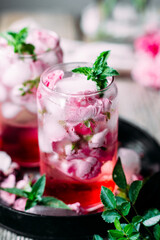 Cold cocktail of rose petals with ice on a wooden table. Rose drink