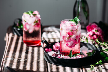 Cold cocktail of rose petals with ice on a wooden table. Rose drink