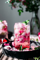 Cold cocktail of rose petals with ice on a wooden table. Rose drink