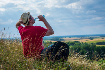 Naklejka na ściany i meble Traveler drinks water in the mountains.Hiker with backpack relaxing on top of the mountain in summer sunny day.
