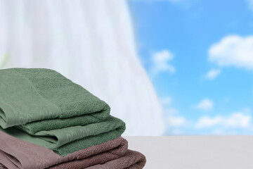 Fototapeta na wymiar Closeup of a stack or pile of brown and green soft terry bath towels on a light table on an abstract blurred blue sky background with copy space for your product presentation montage.