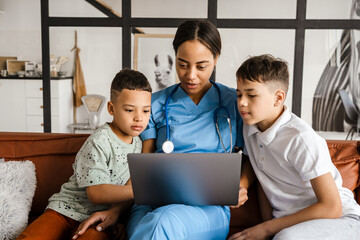 Black woman doctor and her sons using laptop while sitting on couch