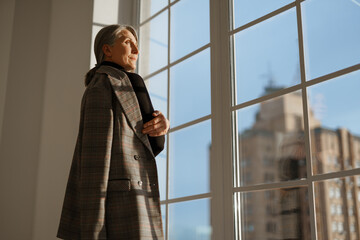 European senior woman with grey hair looking out window