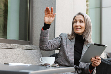 Grey white senior woman gesturing while using tablet computer in cafe