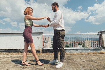 Young dancing couple dance on a rooftop of a building on a sunny day.